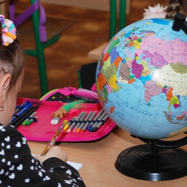 Ein Mädchen sitzt am Schultisch mit Globus