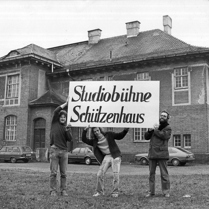 Drei junge Männer halten ein Schild hoch, auf dem "Studiobühne Schützenhaus" steht.