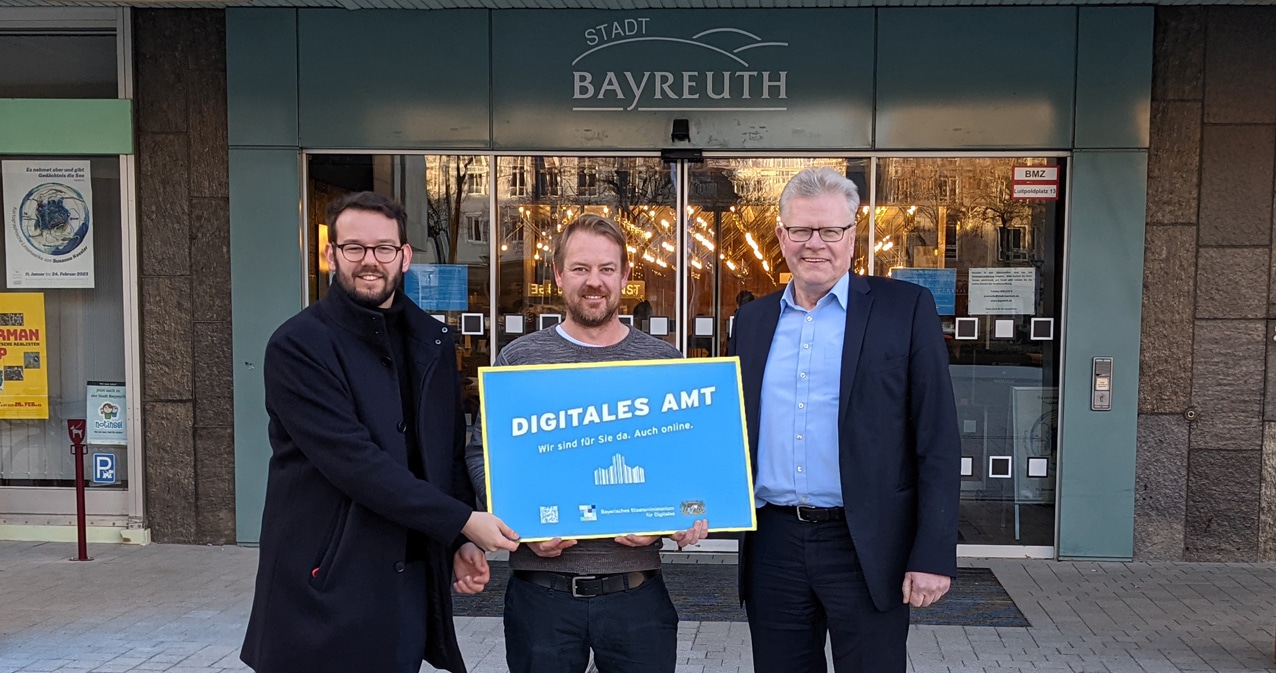 Bürgermeister Zippe, Mitarbeiter Kollenda und Oberbürgermeister Ebersberger präsentieren die Plakette "Digitales Amt" vor dem Eingang des Rathauses.