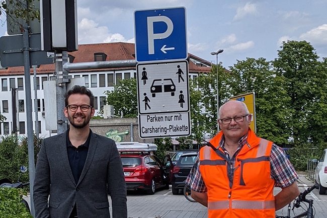 Dr. Zippel und Herr Sellheim stehen auf einem Carsharing-Parkplatz