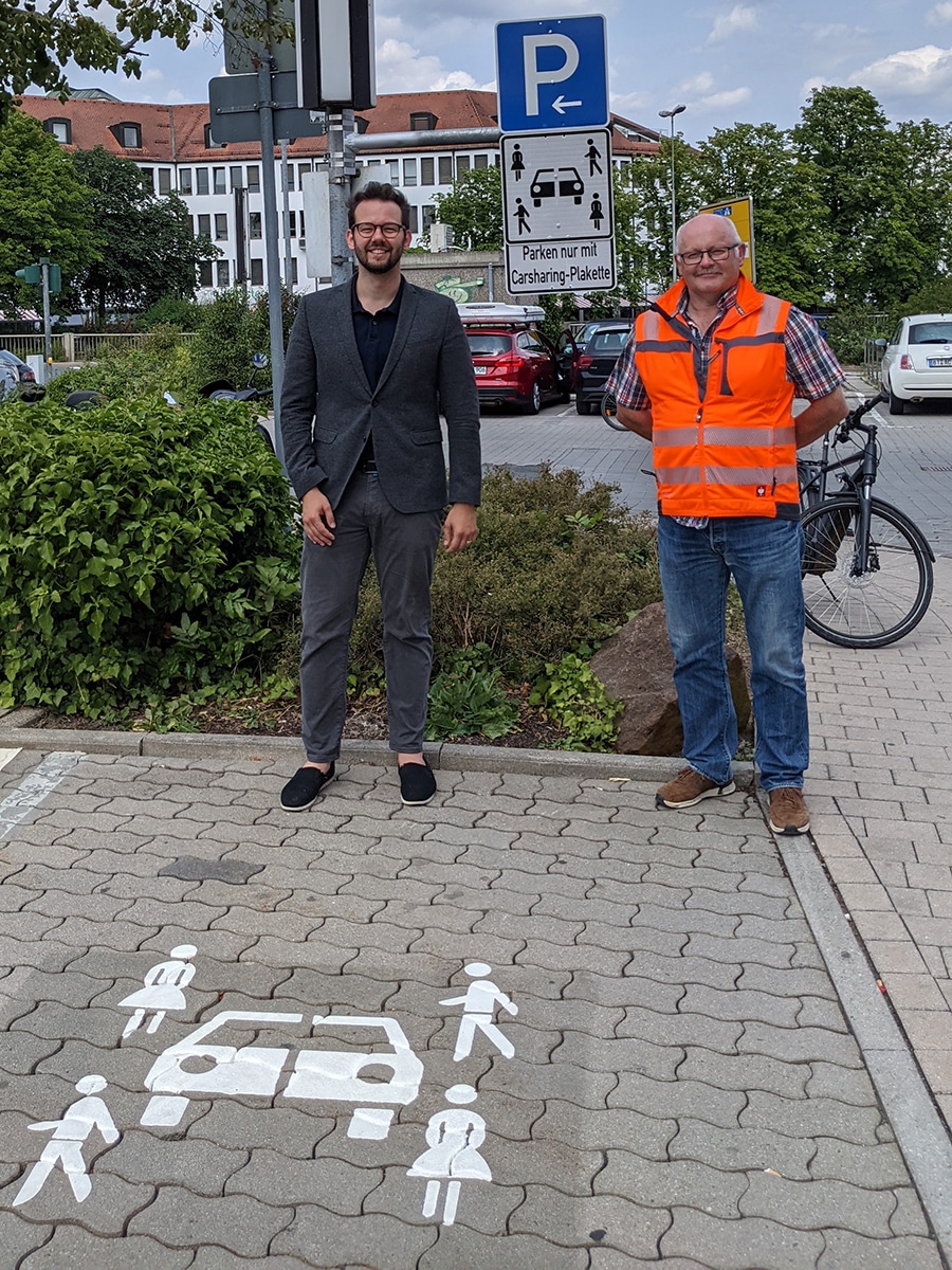 Dr. Zippel und Bernd Sellheim stehen auf einem Carsharing-Parkplatz