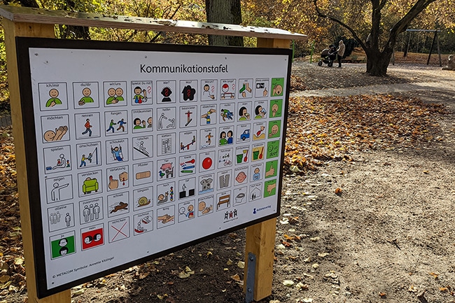 In der linken Bildhälfte steht die Tafel, rechts im Hintergrund ist der Spielplatz zu erkennen