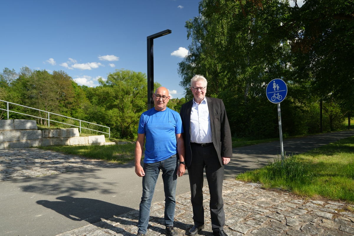 Zwei Männer stehen an einem Radweg unter einer Straßenleuchte