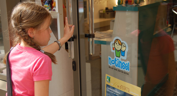 Ein Mädchen steht vor einer Glastür mit einem "Notinsel"-Logo.
