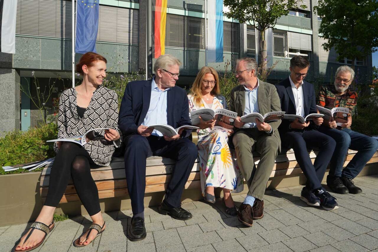 Sechs Personen sitzen auf einer Bank vor dem Rathaus und blätttern in einem Magazin. | Foto: Stadt Bayreuth