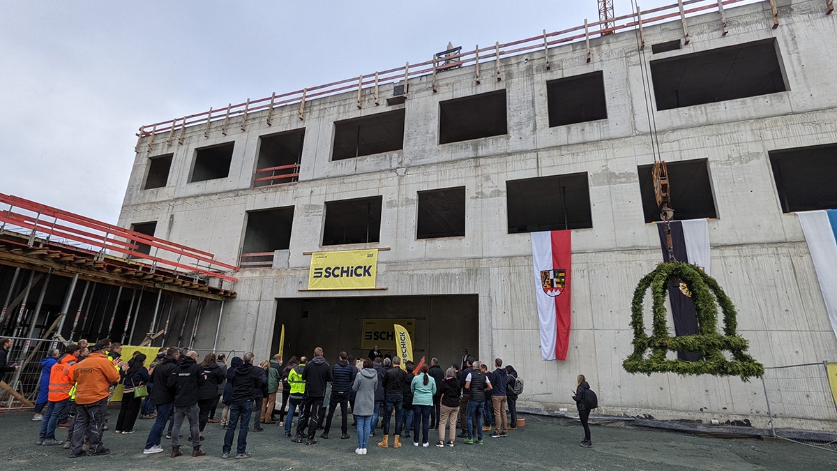 Menschen stehen vor dem Rohbau, rechts hängt die Richtkrone vom Kran herunter