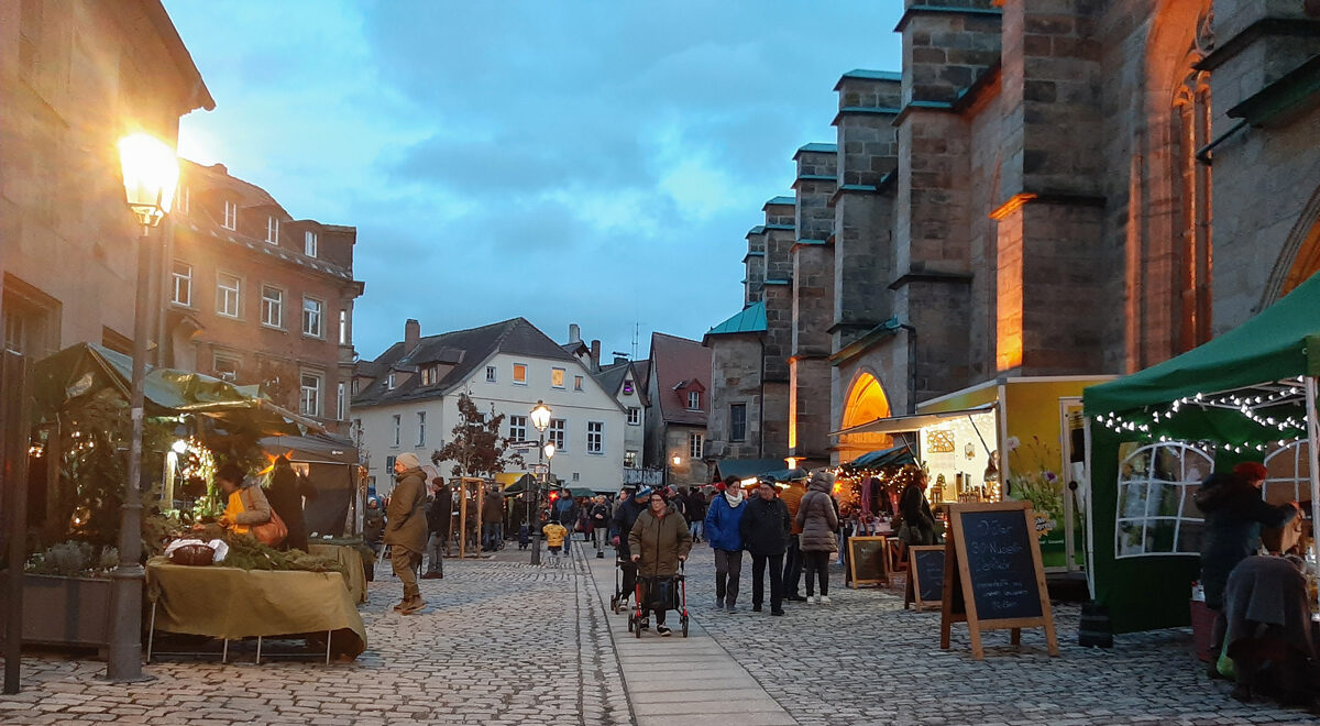 Das Bild zeigt einen Weihnachtsmarkt in einer historischen Innenstadt neben einer Kirche.