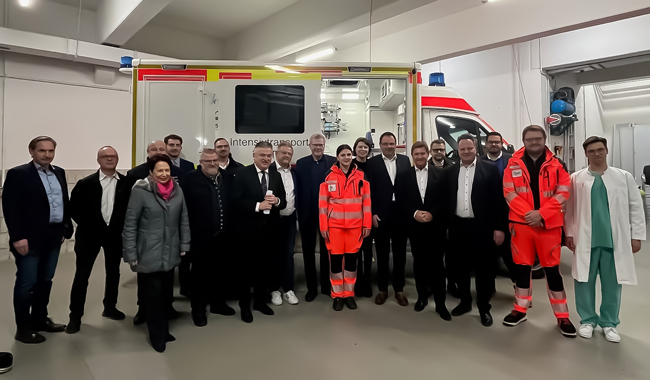 Eine Gruppe Personen steht in einer Garage vor einem Rettungsfahrzeug.