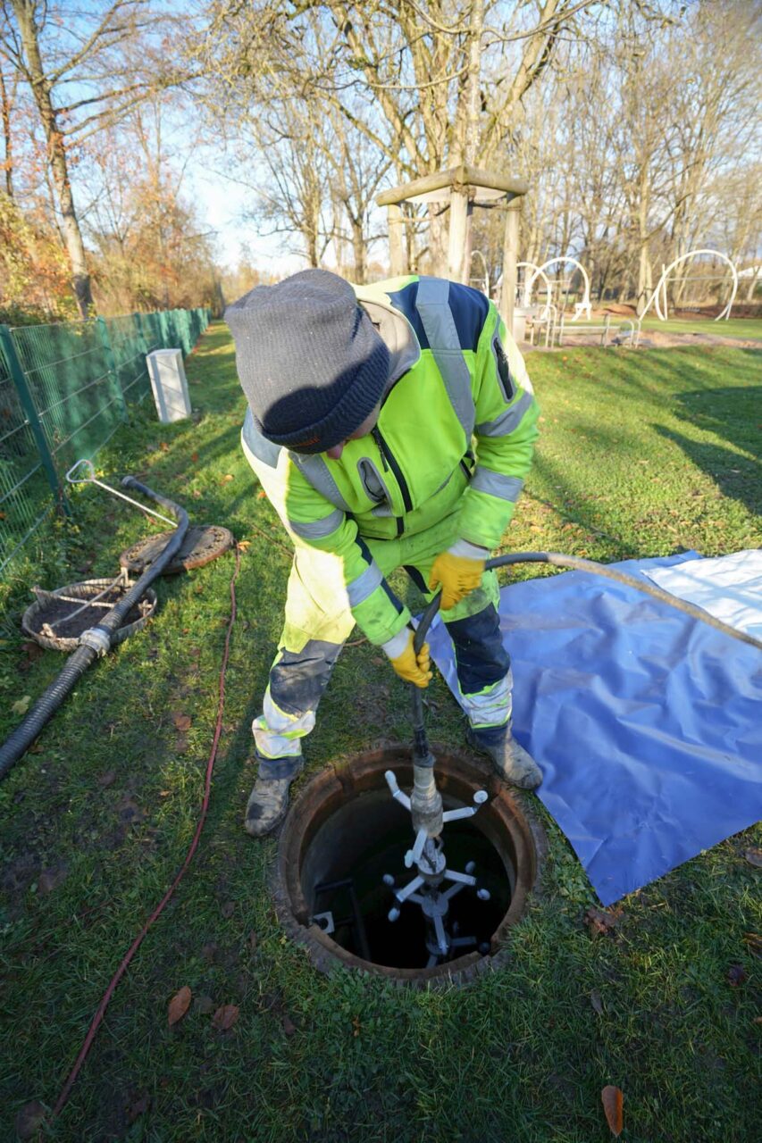 Ein Arbeiter zieht einen Lampenzug in einen Kanalschacht.