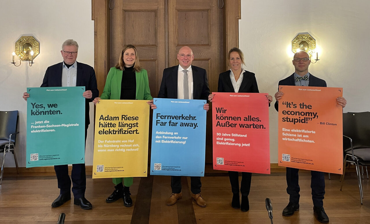 Drei Männer und zwei Frauen halten farbige Plakate hoch.