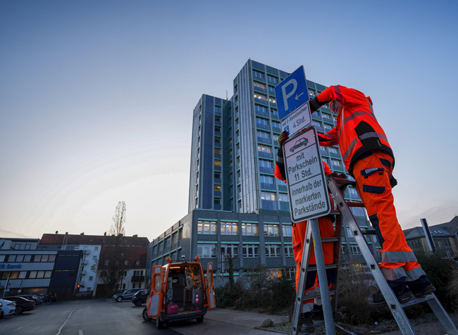 Zwei Mitarbeiter des Stadtbauhofs bringen ein Verkehrsschild vor dem Rathausparkplatz an.