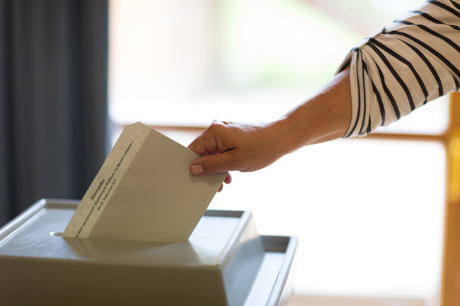 Ein Stimmzettel wird in eine Wahlurne eingeworfen.