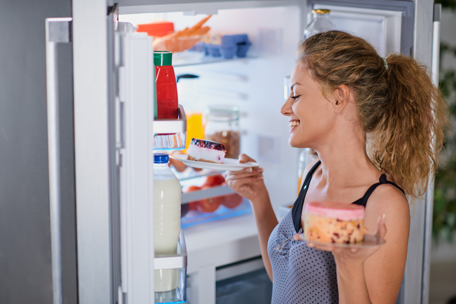 Eine junge Frau guckt in einen Kühlschrank